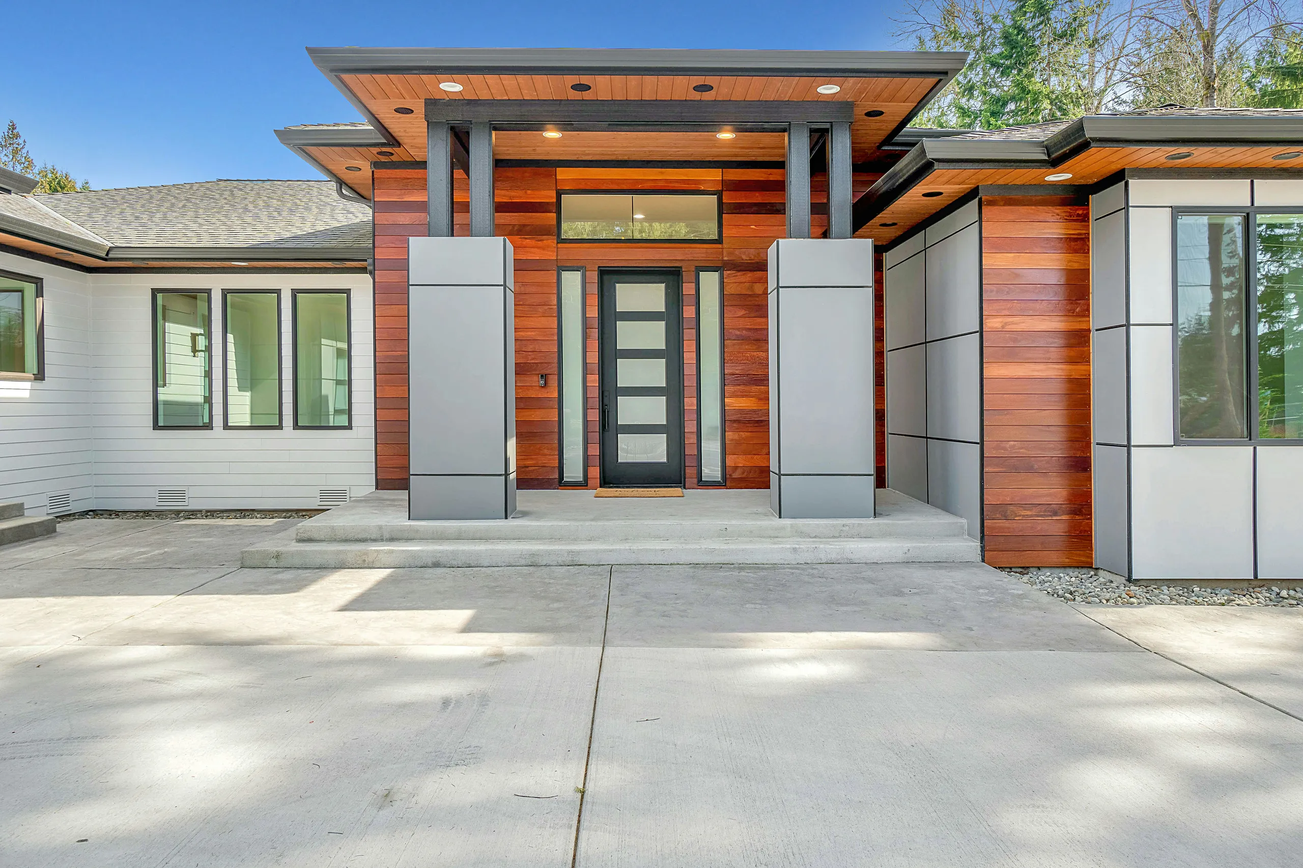 Casa moderna con fachada de madera, puerta de entrada oscura y acceso de hormigón