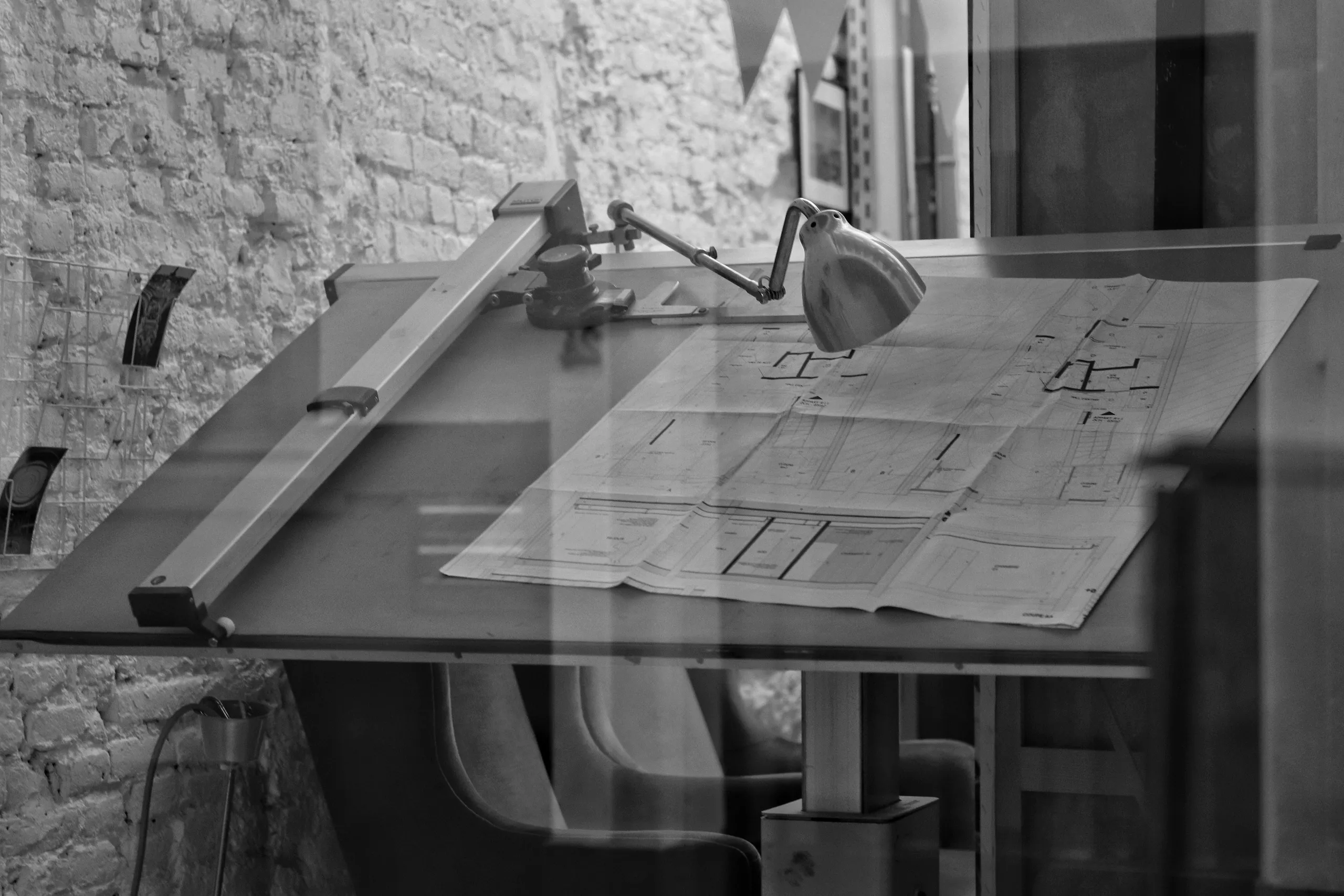 Mesa de dibujo con un plano arquitectónico y una lámpara en el estudio